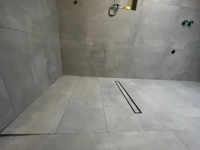 Bodengleiche Dusche mit Duschrinne und großformatigen grauen Fliesen im Rohbau